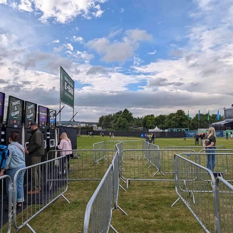 Six mobile EBar units serve a range of different drinks at a greenfield event with a stage set up in the background