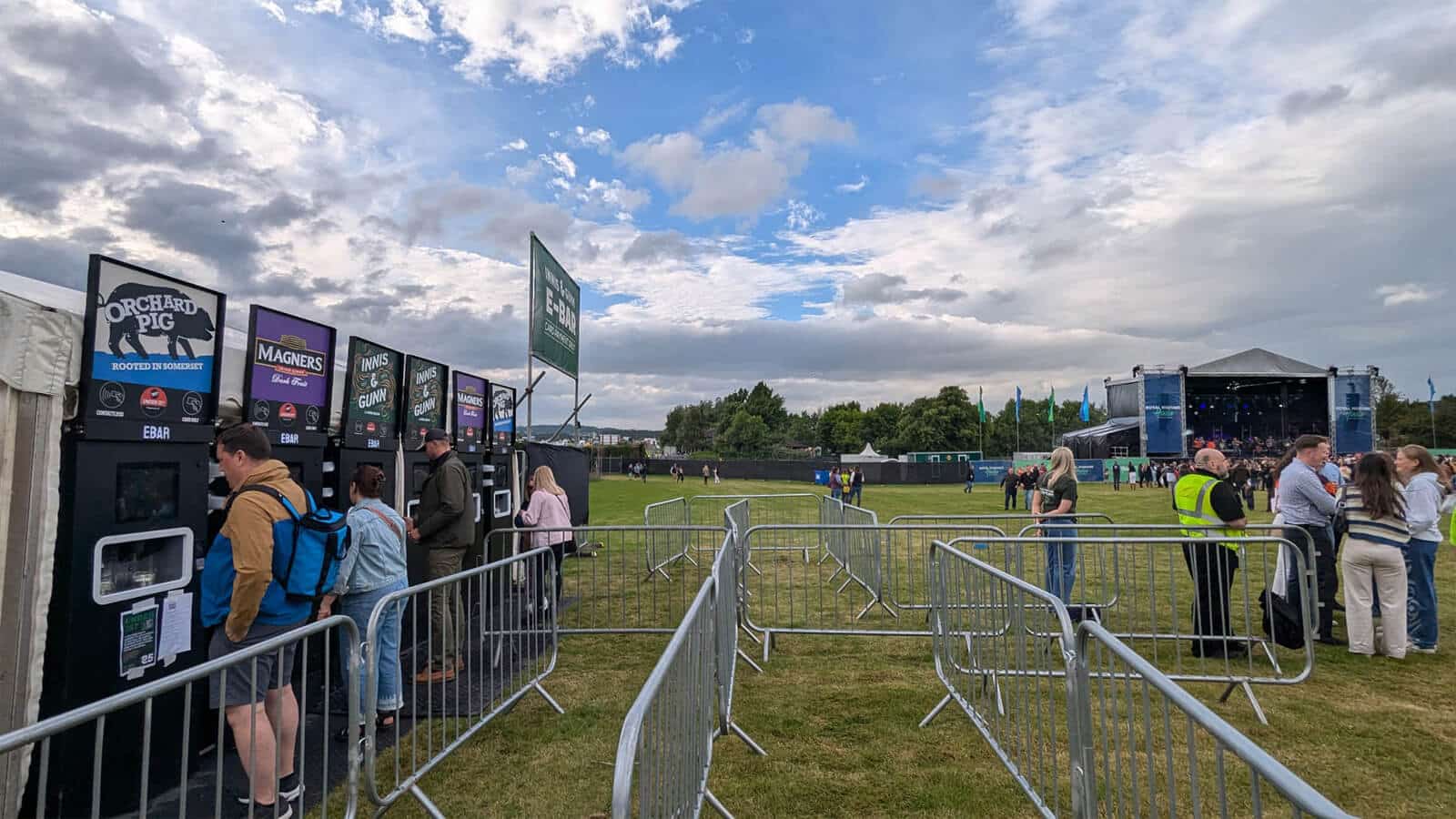 Six mobile EBar units serve a range of different drinks at a greenfield event with a stage set up in the background