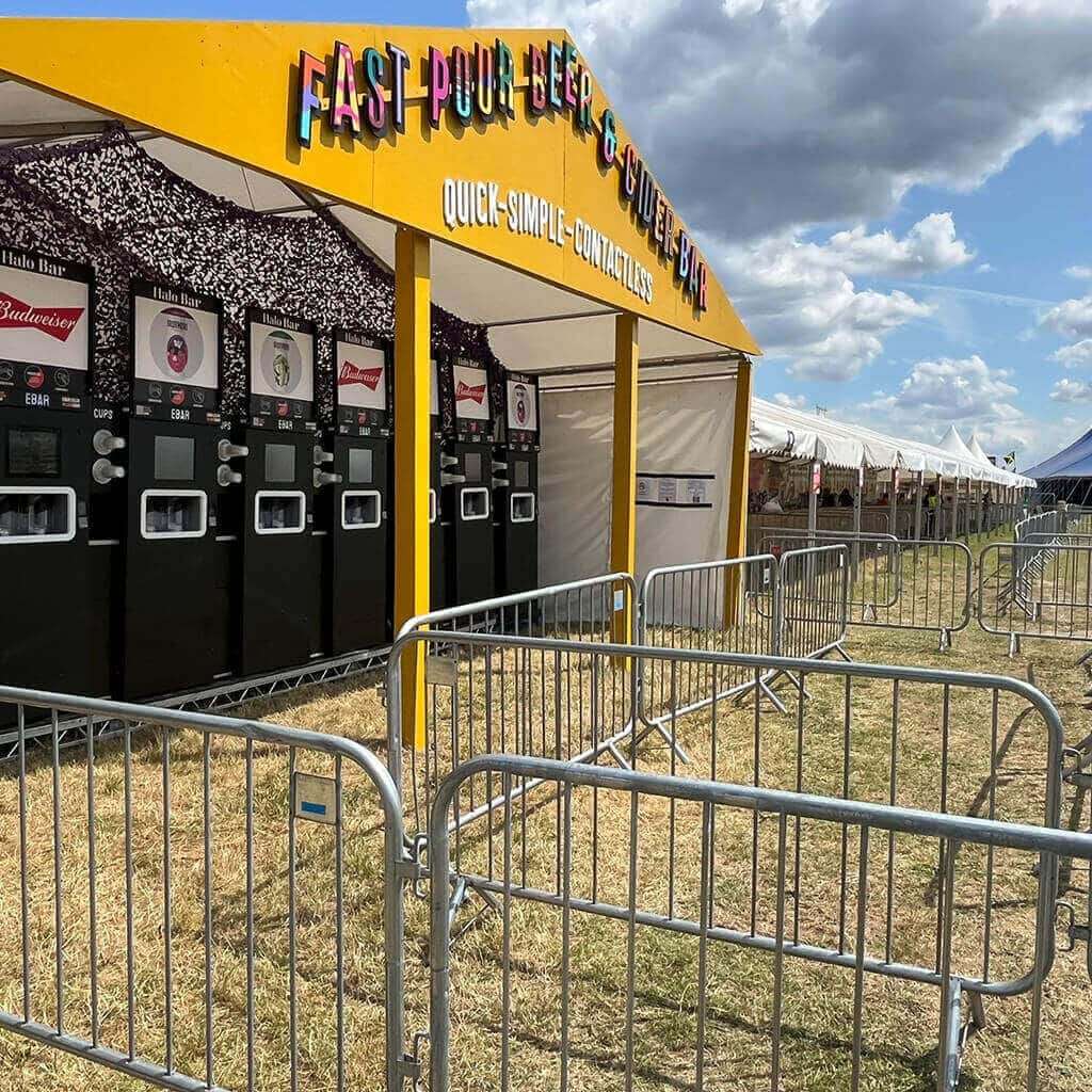 Eight mobile EBar units under a yellow shelter on a greenfield event, stand ready to pour a range of drinks.