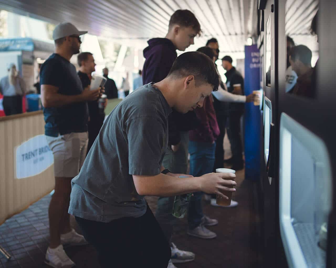 A man takes his pint from the chamber of a mobile EBar at Trent Bridge Stadium, Nottingham as other fans in the background order their own